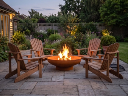 Corten steel fire bowl with chairs around it in a backyard at dusk
