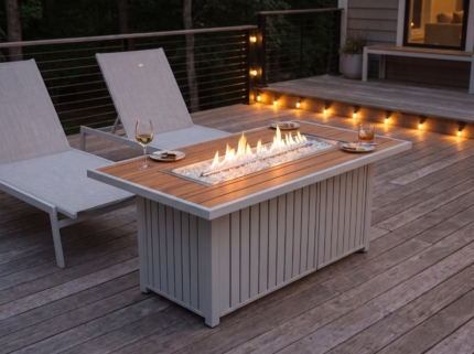 Teak-look fire pit table between lounge chairs at dusk